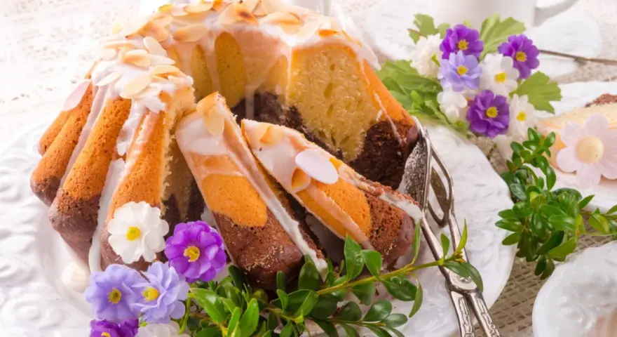 Modne ciasta na Wielkanoc: marmurkowa babka z lukrem i migdałami, ozdobiona wiosennymi kwiatami i zielenią.