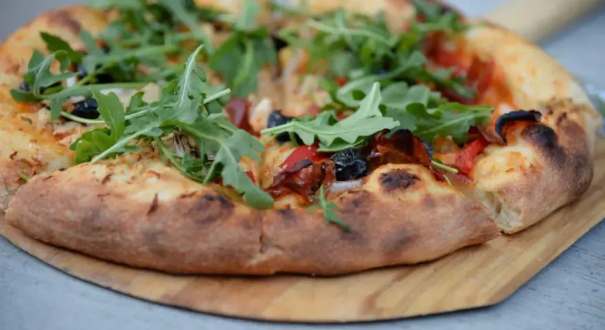 Pyszna pizza z rukolą i oliwkami na drewnianej desce. Proste ciasto na pizzę zawsze wychodzi, tworząc idealną bazę dla ulubionych dodatków.