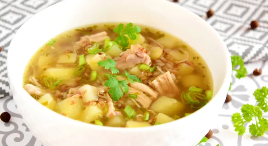 Aksamitny krupnik na rosole z kawałkami mięsa, ziemniaków i zielonej cebulki, udekorowany natką pietruszki.