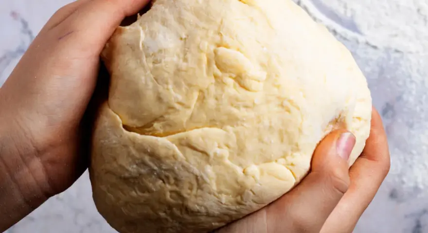 Dłonie formują puszyste ciasto drożdżowe na suchych drożdżach, gotowe do pieczenia.