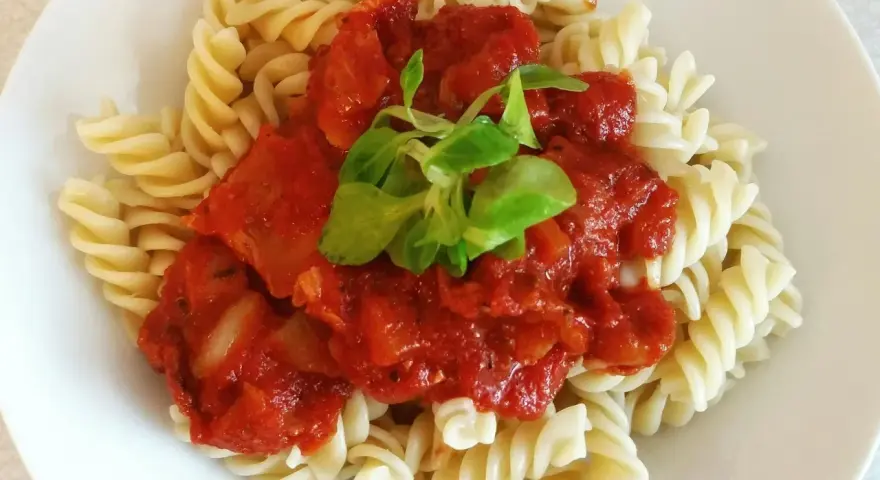 Fusilli z sosem pomidorowym i pomidorkami koktajlowymi, udekorowane świeżą zieleniną. Pyszne danie gotowe w kilka minut.