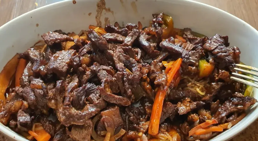 Pyszne wołowina stir fry z warzywami i makaronem, podane w białej misce.