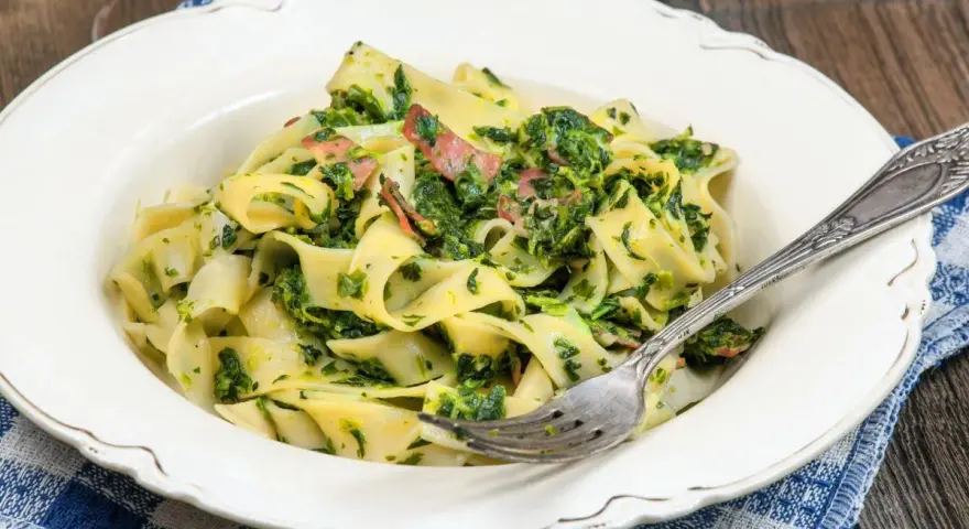 Pappardelle z boczkiem i szpinakiem, danie pełne smaku, podane na talerzu z widelcem.