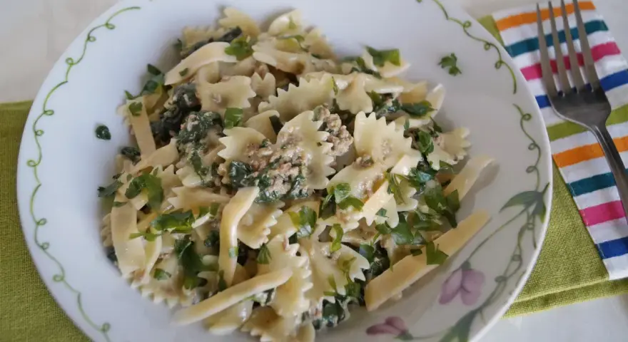 Pyszny makaron z pesto i tuńczykiem, posypany świeżą natką pietruszki, podany na talerzu z ozdobnym brzegiem.