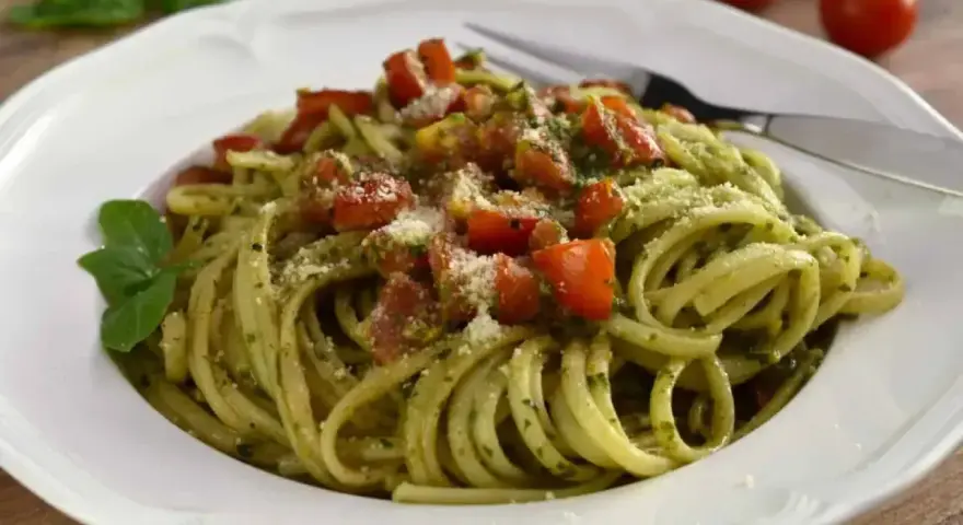 Pyszny makaron z pesto, pomidorkami i parmezanem, udekorowany listkiem bazylii. Idealny na szybki obiad.