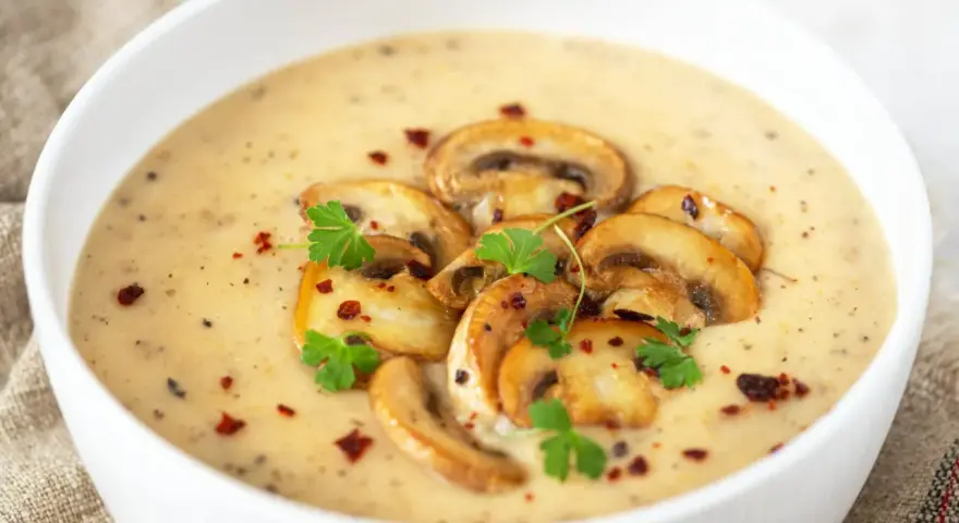 Aksamitny zupa krem z pieczarek, udekorowana plasterkami pieczarek, natką pietruszki i płatkami chili. Idealna na chłodne dni.