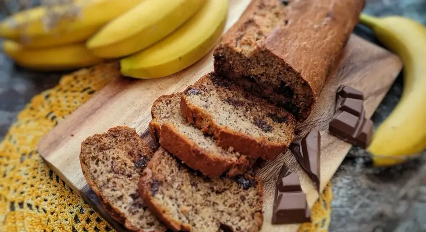 Pyszny chlebek bananowy z czekoladą, pokrojony na kromki, obok świeże banany i kawałki czekolady.