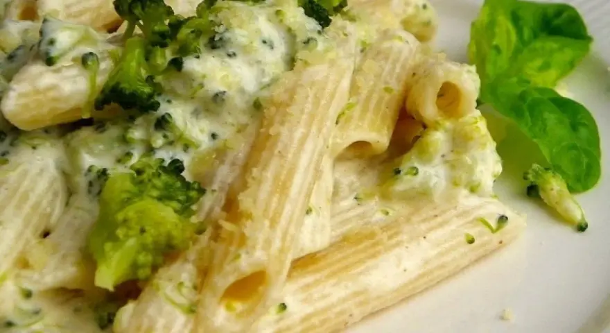 Penne z brokułami w kremowym sosie serowym, udekorowane listkiem bazylii. Pyszne danie, które zachwyci każdego smakosza.