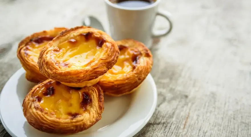 Na talerzyku leżą trzy chrupiące pastéis de nata, obok filiżanka kawy. Idealny poranek.