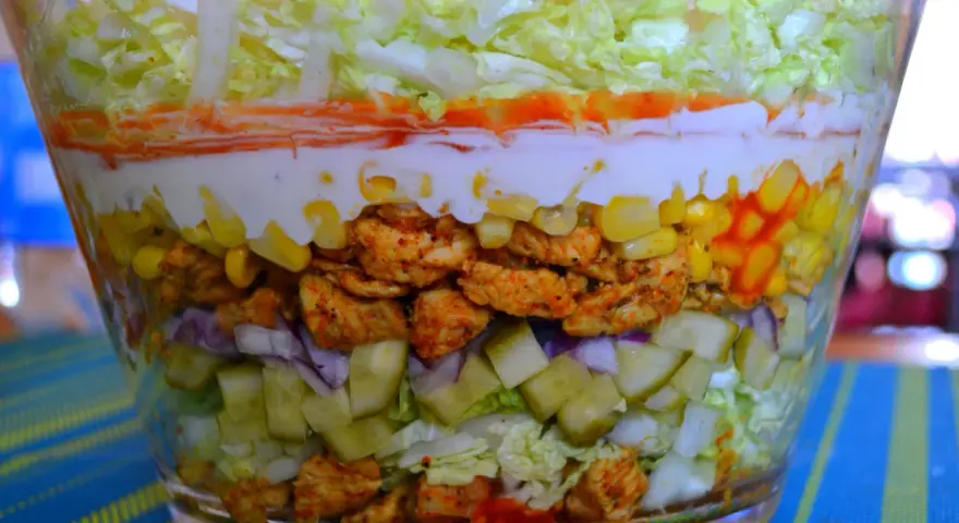 Warstwowa sałatka z kurczakiem w stylu gyros, z kukurydzą, ogórkiem, cebulą i sosem.