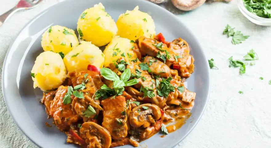 Gulasz drobiowy z pieczarkami i ziemniakami na talerzu, ozdobiony natką pietruszki.