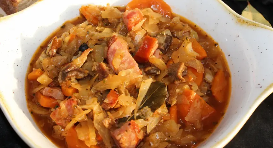 Pyszny bigos ze słodkiej kapusty z kiełbasą i marchewką, podany w białej misie.