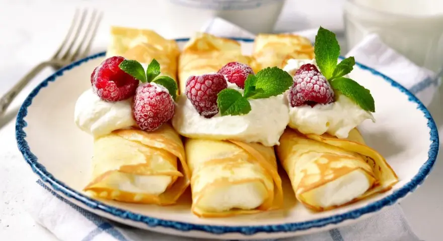 Rolowane naleśniki z mascarpone, udekorowane malinami i miętą, wyglądają apetycznie.
