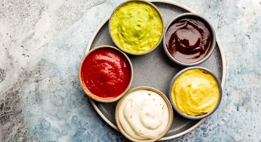 Sześć miseczek z sosami: zielony guacamole, czerwony ketchup, ciemny barbecue, żółta musztarda i biały majonez. Idealne do dań, gdy zastanawiasz się, jak zrobić sos.