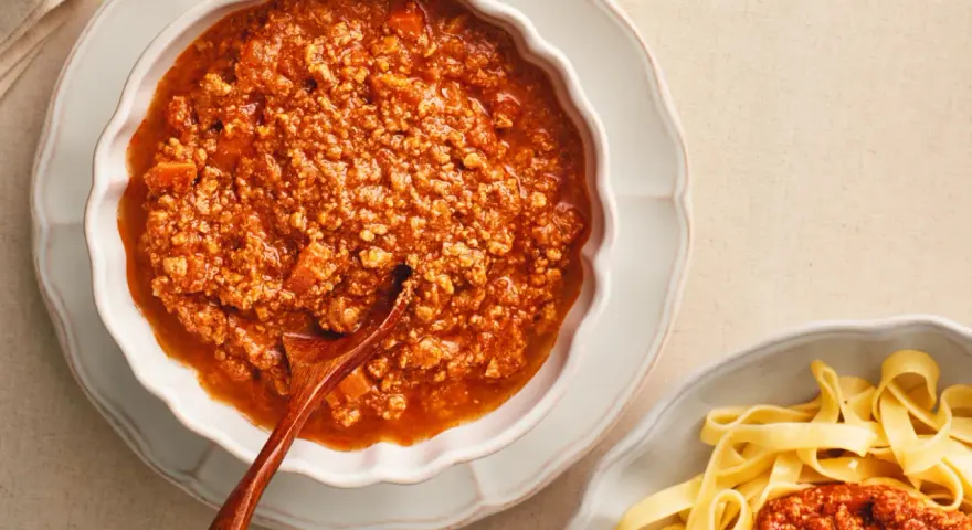 Gęsty, aromatyczny sos do spaghetti bolognese w miseczce, obok porcji makaronu tagliatelle.