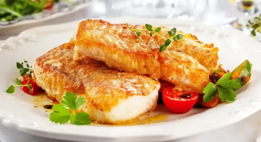 Dwa soczyste filety ryby pieczonej w piekarniku w folii, podane z pomidorkami i ziołami.