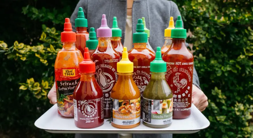 Taca z wieloma butelkami sosu Sriracha o różnych kolorach nakrętek.