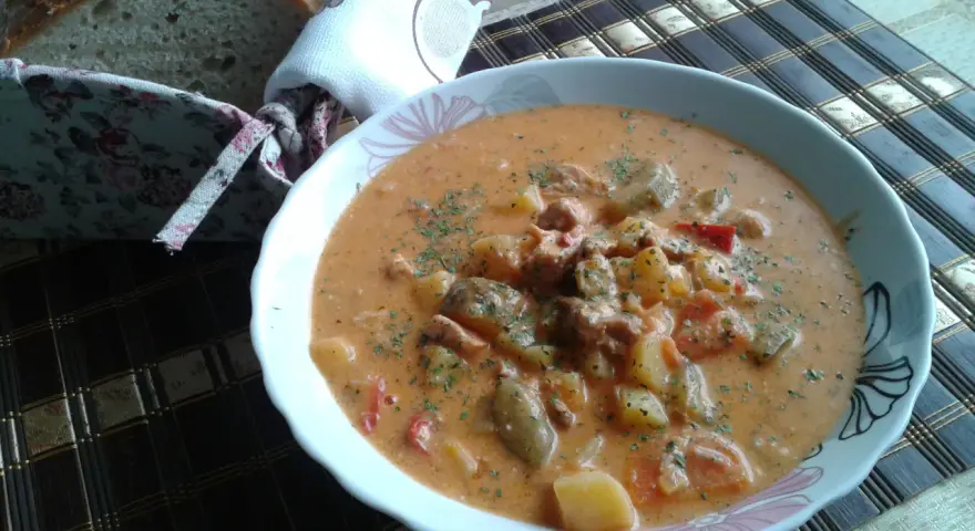 Pyszny bogracz z pieczarkami, ziemniakami i mięsem, posypany natką. Obok koszyk z chlebem.