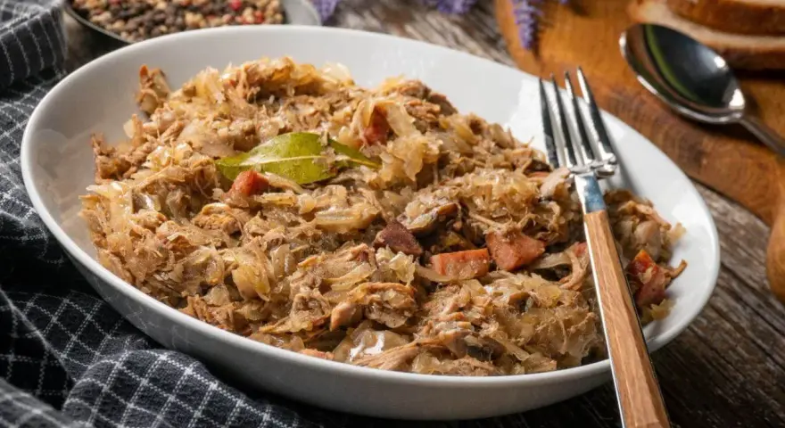 Pyszny bigos w białej misce, z widelcem. Zastanawiasz się, ile może stać bigos w lodówce? Nawet kilka dni, a smakuje coraz lepiej!