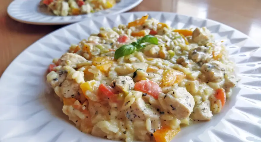 Pyszne risotto z kurczakiem i kolorowymi warzywami, udekorowane listkiem bazylii. Idealne na obiad.