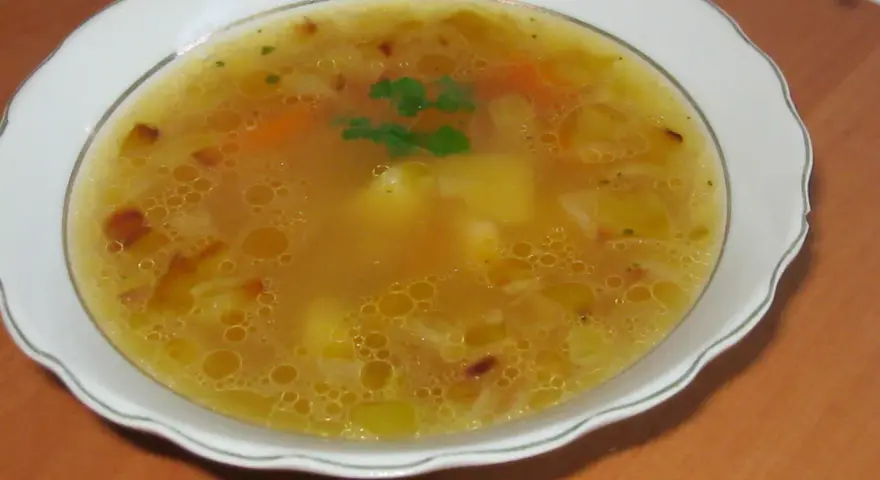 Prosta zupa cebulowa z ziemniakami, z kawałkami marchewki i natką pietruszki, podana w białej misce.