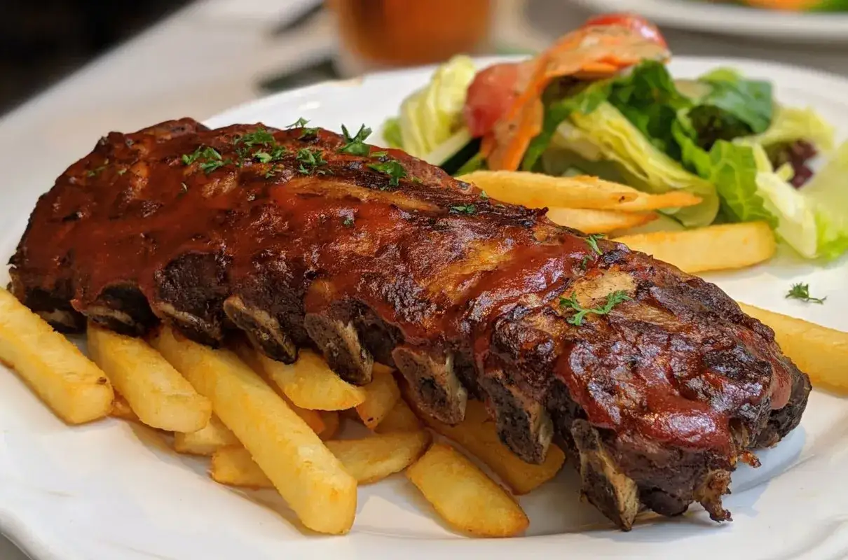 Soczyste żeberka w sosie barbecue, podane z chrupiącymi frytkami i świeżą sałatką. Idealne danie dla miłośników mięsa.