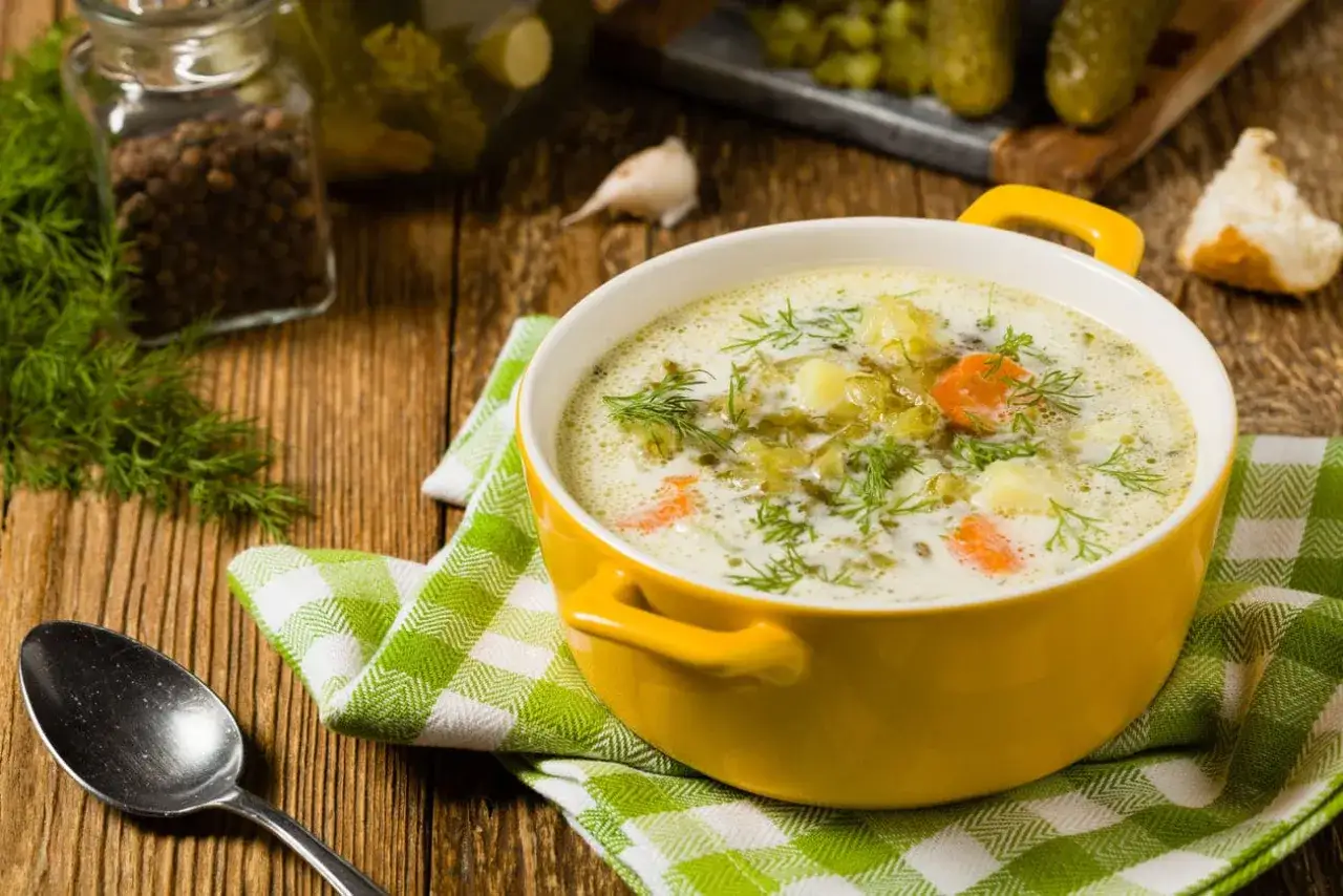 Zupa ogórkowa z koperkiem, ziemniakami i marchewką. Obok słoik z pieprzem, czosnek i ogórki. Idealne przyprawy do zupy ogórkowej to sekret smaku.