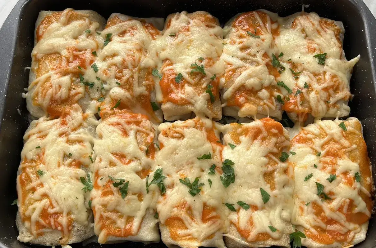 Zapiekane naleśniki z pieczarkami, polane sosem pomidorowym i posypane ciągnącym się serem, udekorowane natką pietruszki.