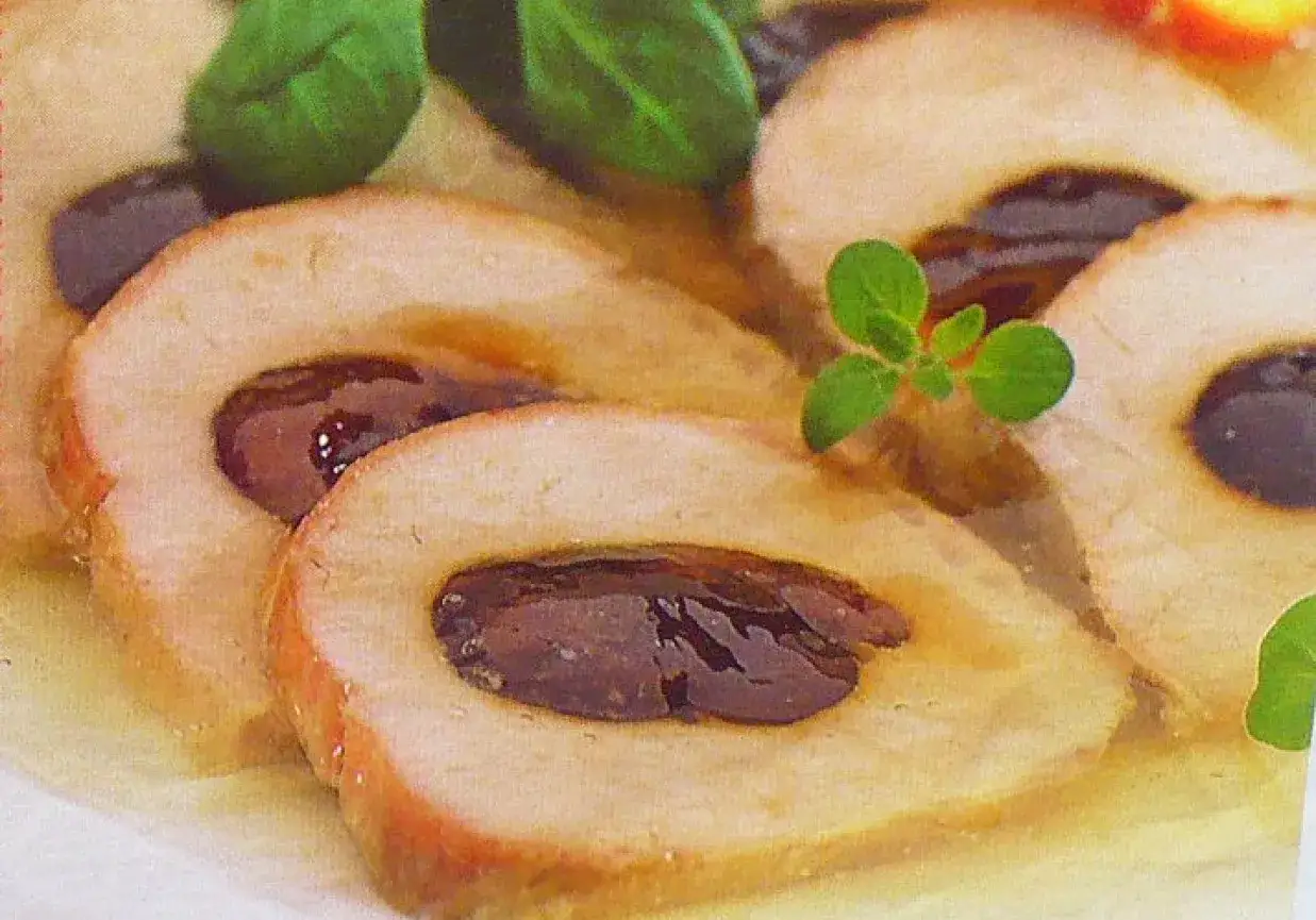 Schab ze śliwką w galarecie, pokrojony w plastry, z zielonymi listkami ziół.