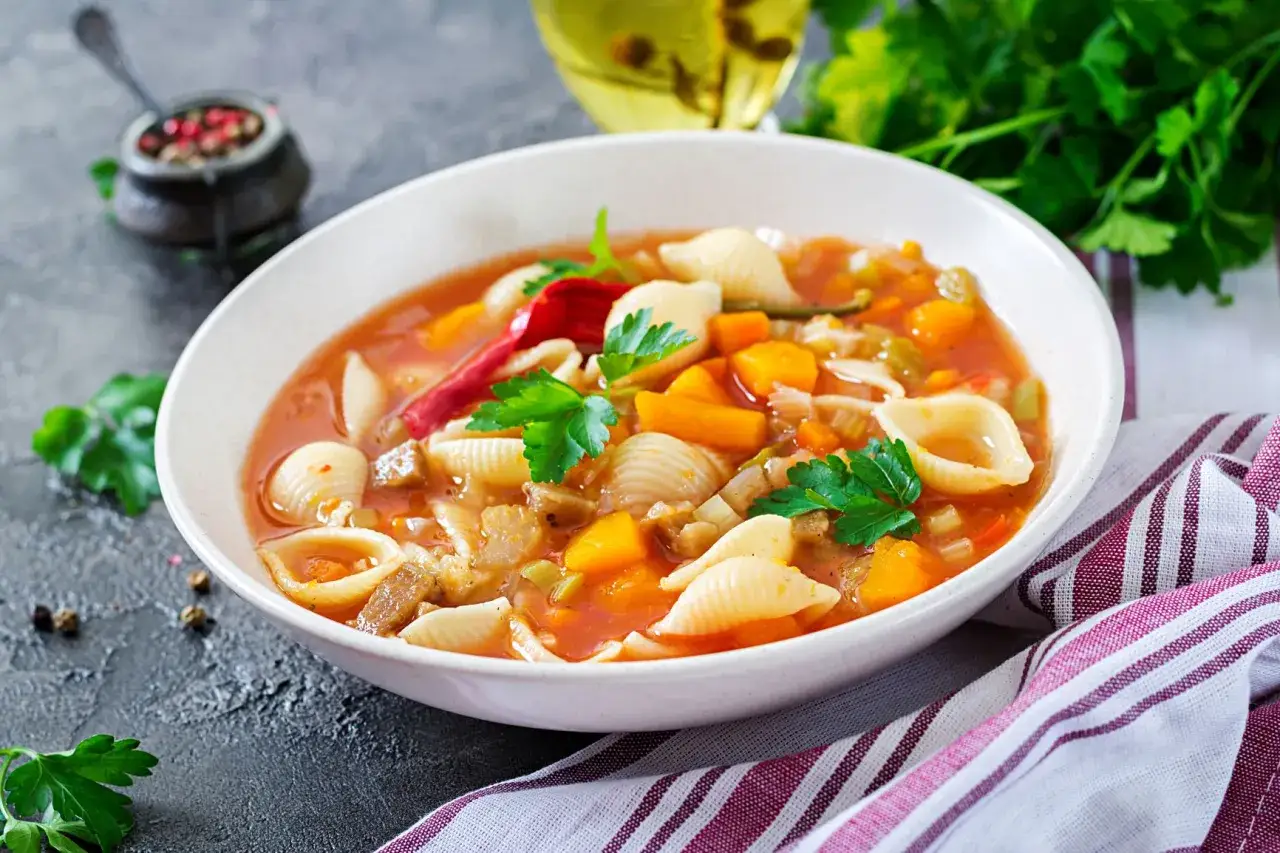 A miska pełna aromatycznej zupy minestrone, z makaronem muszelki, warzywami i ziołami. Oryginalny przepis na rozgrzewający posiłek.