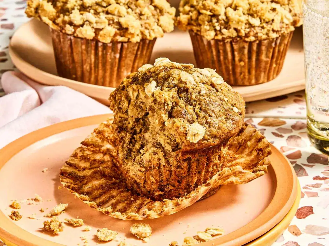 Pyszne muffinki bananowe fit, lekko nadgryzione, z kruszonką na wierzchu, na różowym talerzyku.