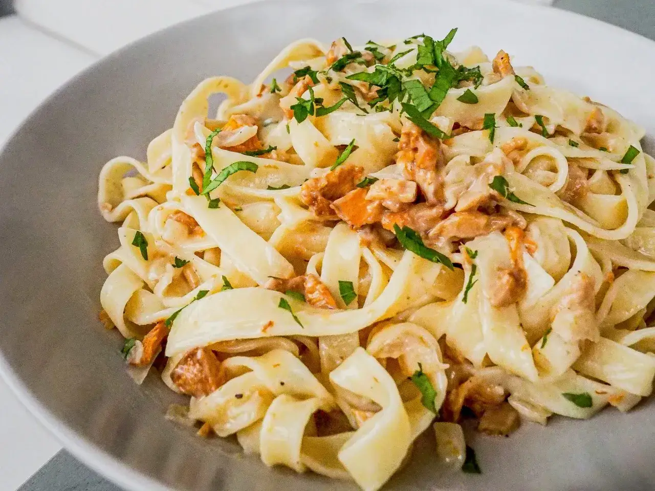 Pyszny makaron tagliatelle z kremowym sosem kurkowym i posiekaną natką pietruszki.