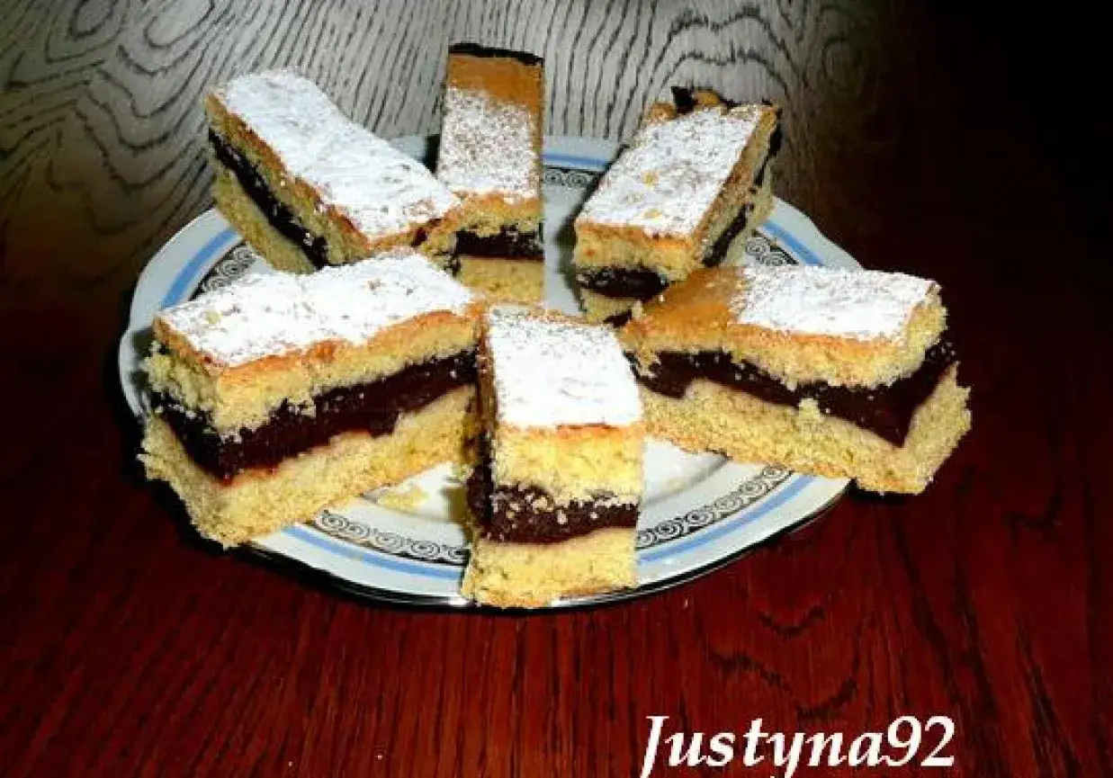Pyszne ciasto z budyniem czekoladowym, posypane cukrem pudrem, prezentuje się apetycznie na talerzu.