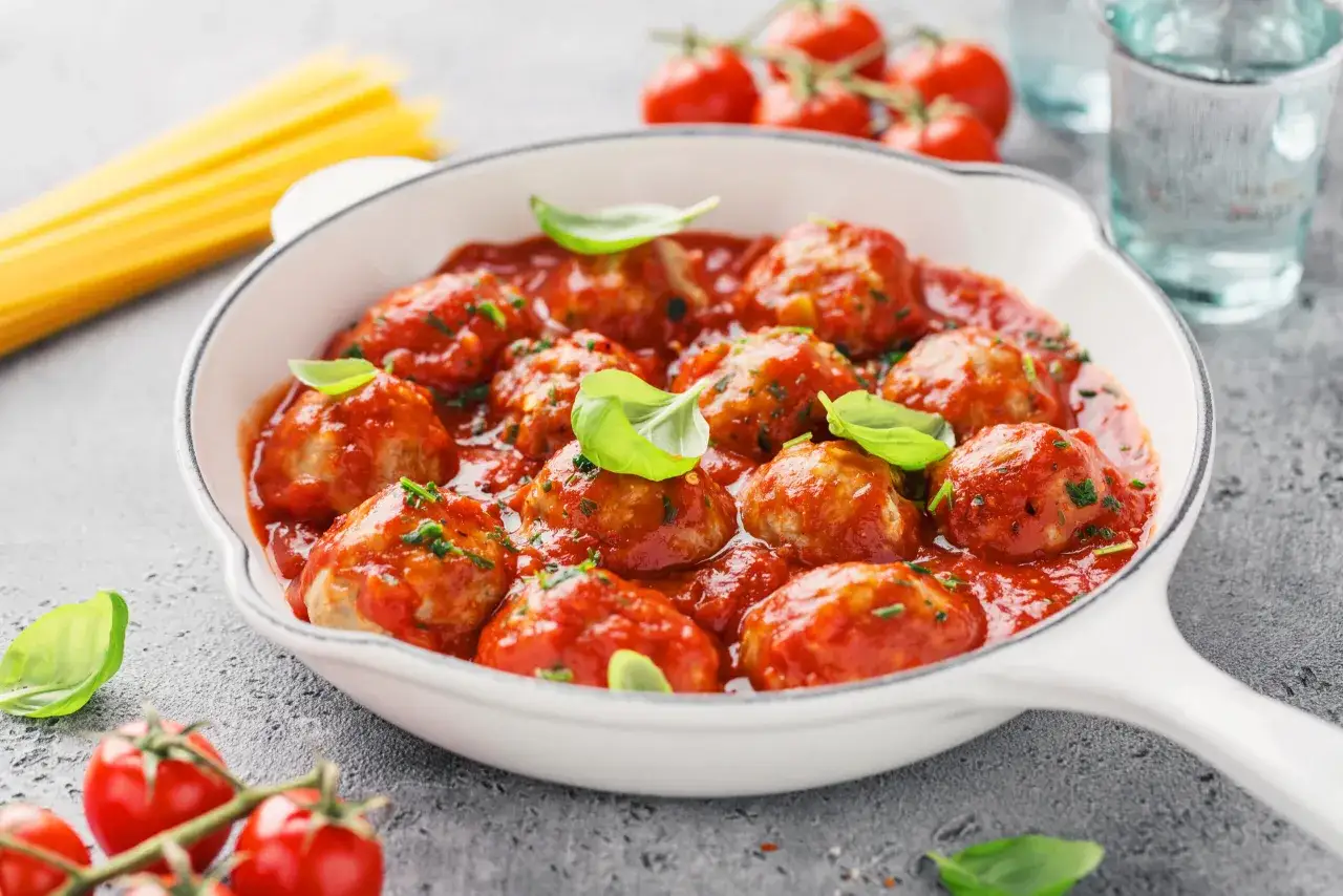 Pyszne pulpeciki w sosie pomidorowym, udekorowane bazylią, gotowe do podania ze spaghetti.