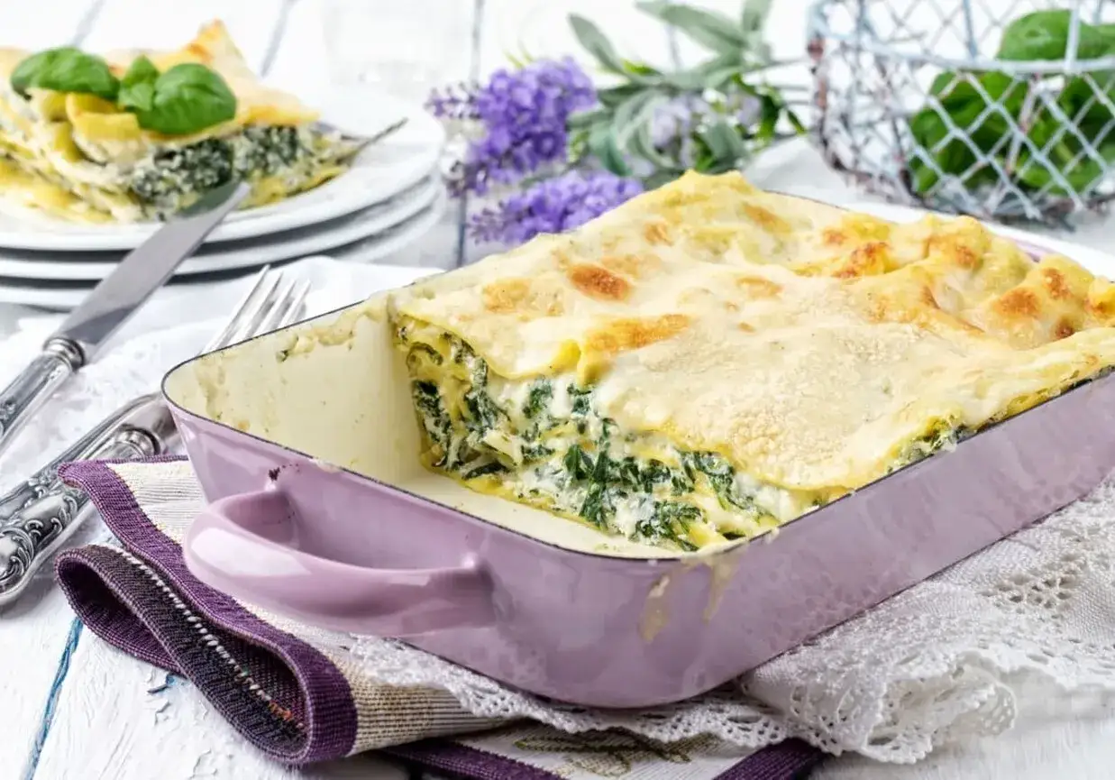 Pyszne lasagne ze szpinakiem i beszamelem, prosto z piekarnika, w fioletowym naczyniu.
