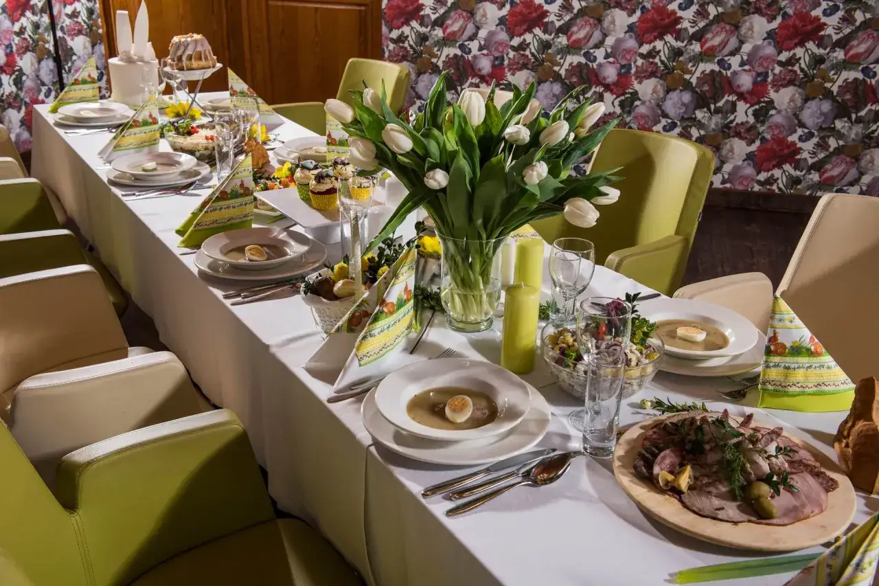 Wielkanocny stół z białymi tulipanami, babeczkami i talerzami z zupą. Na środku półmisek z wędlinami, obok koszyczek z jajkami. To idealna salatka na wielkanoc.