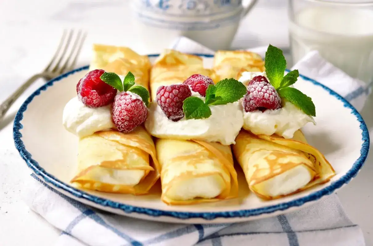 Rolowane naleśniki z mascarpone, udekorowane malinami i miętą, wyglądają apetycznie.