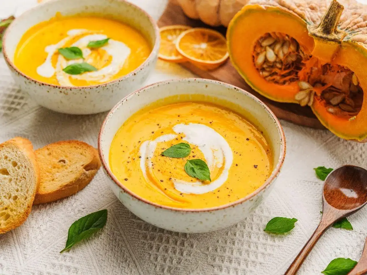 Aksamitna zupa z dyni hokkaido, udekorowana śmietaną i bazylią, podana z grzankami. Obok poł&oacute;wka dyni.