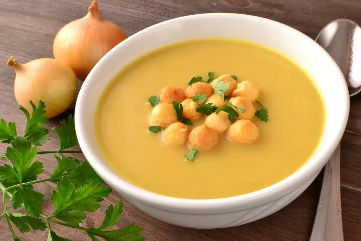 Prosta zupa cebulowa z ziemniakami, ozdobiona grzankami i natką pietruszki, obok leżą cebule.