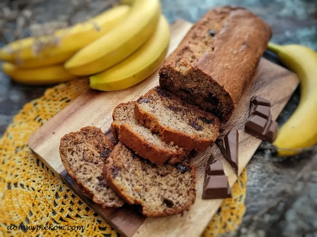 Pyszny chlebek bananowy z czekoladą, pokrojony na kromki, obok leżą banany i czekolada.