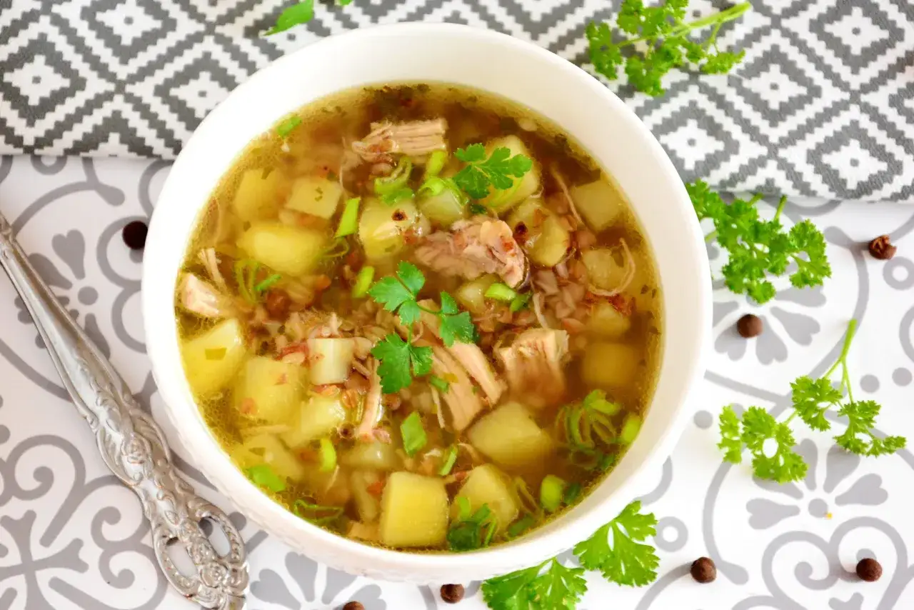 Aromaticzny krupnik na rosole z kawałkami mięsa, ziemniakami i zieloną cebulką, udekorowany natką pietruszki.