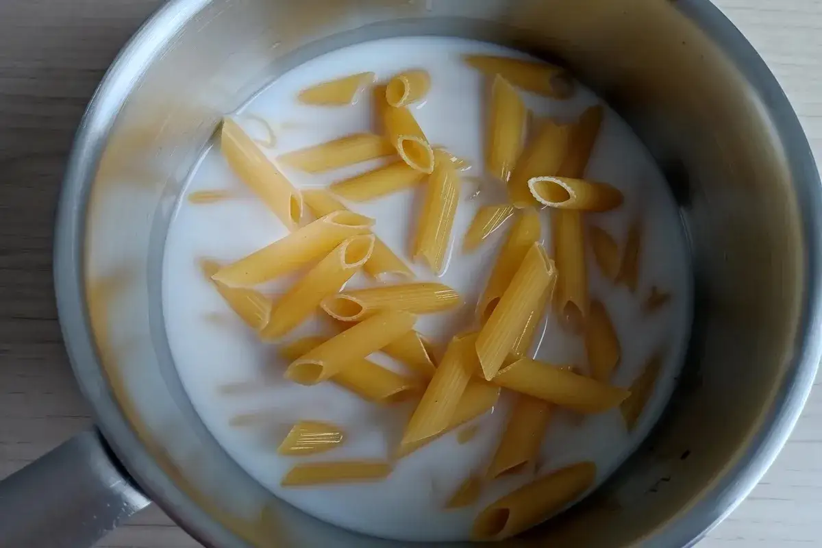 Makaron penne gotuje się w mleku w metalowym garnku.