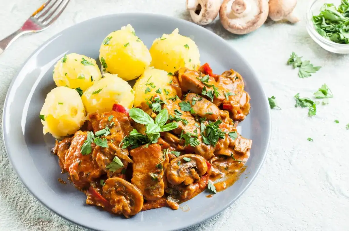 Gulasz drobiowy z pieczarkami, podany z ziemniakami, posypany natką pietruszki. Pyszne danie na obiad.