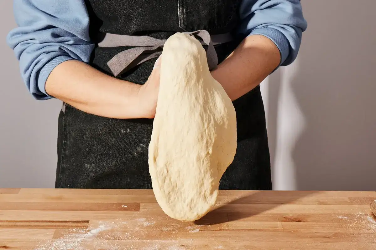 Ręce formują puszyste ciasto na pizzę, które wisi swobodnie, gotowe do pieczenia.