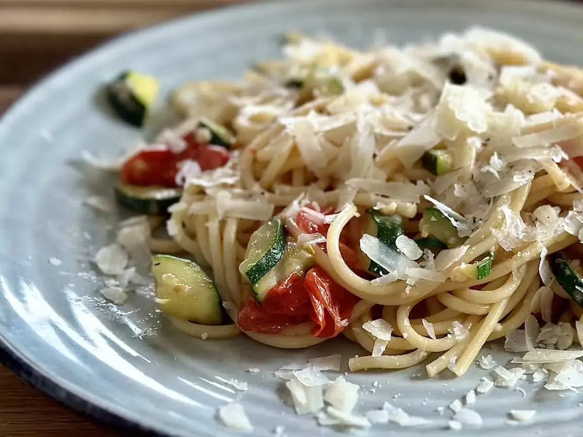 Pyszny makaron z pomidorkami koktajlowymi i cukinią, posypany parmezanem.