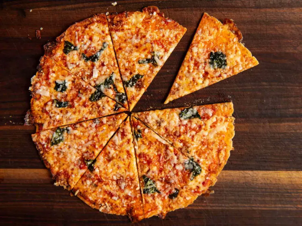 Chrupiąca pizza z tortilli, pokrojona w trójkąty, z roztopionym serem i zielonymi listkami bazylii.