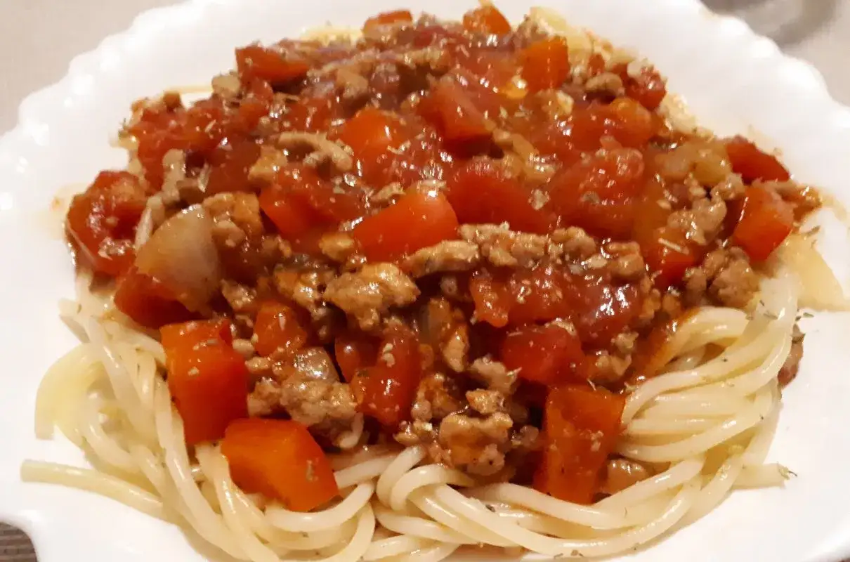 Pyszne spaghetti z mięsem mielonym i pomidorami, podane na białym talerzu.