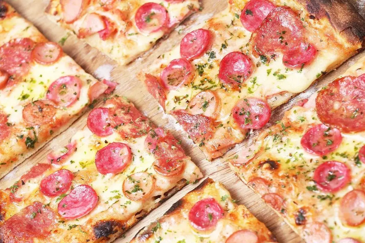 Kawałki pizzy z kiełbasą i serem, posypane ziołami. Proste ciasto na pizzę zawsze wychodzi, idealne na szybki obiad.