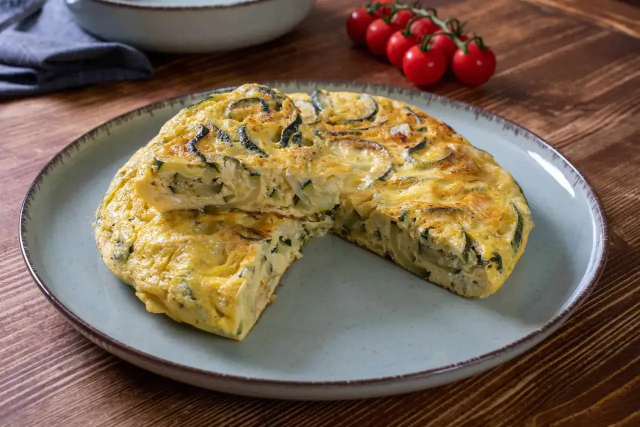 Pyszna frittata z cukinią, podana na talerzu, z pomidorkami koktajlowymi w tle.