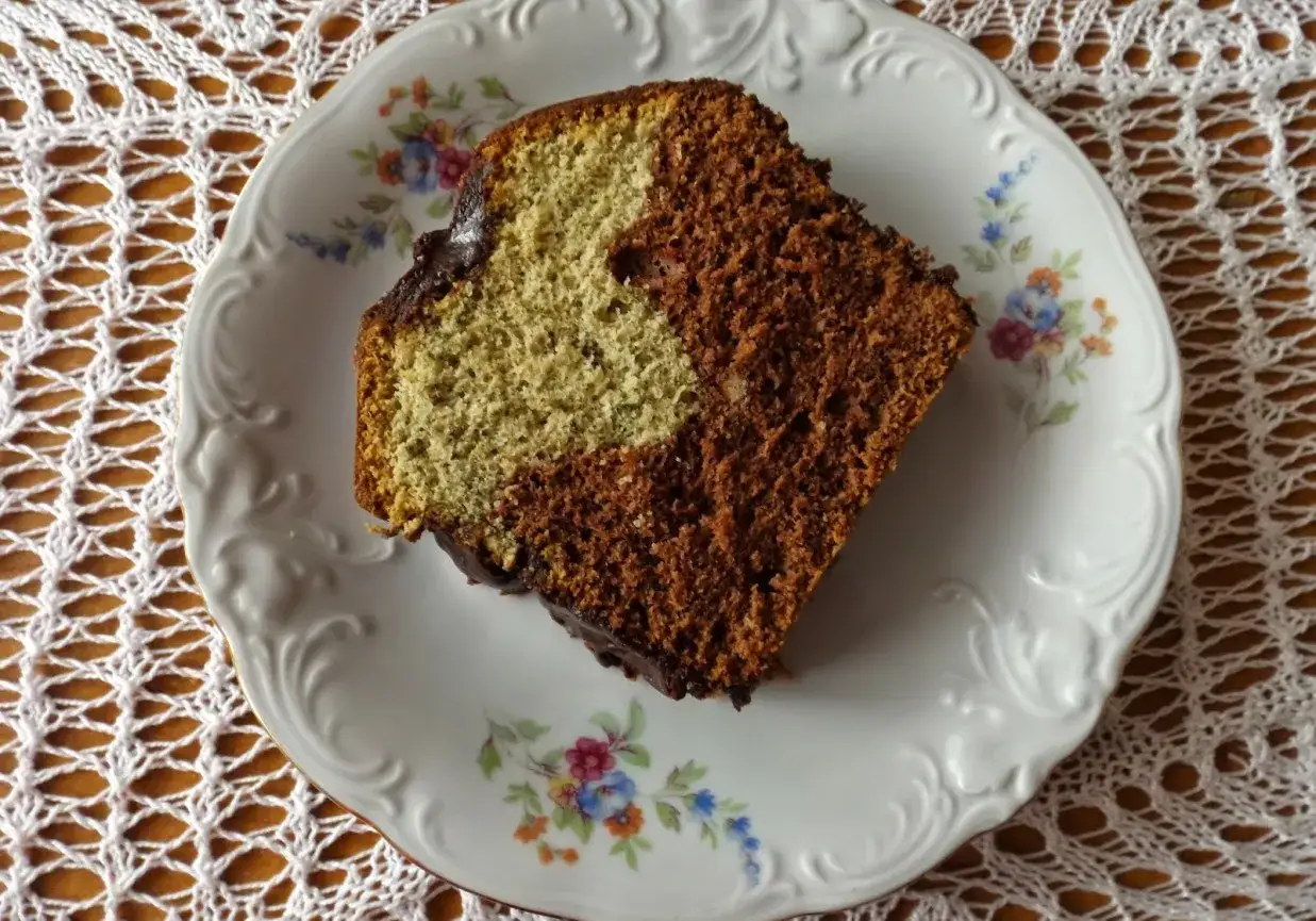 Szybka babka z majonezem i kakao, dwukolorowa, z polewą czekoladową, na ozdobnym talerzyku.